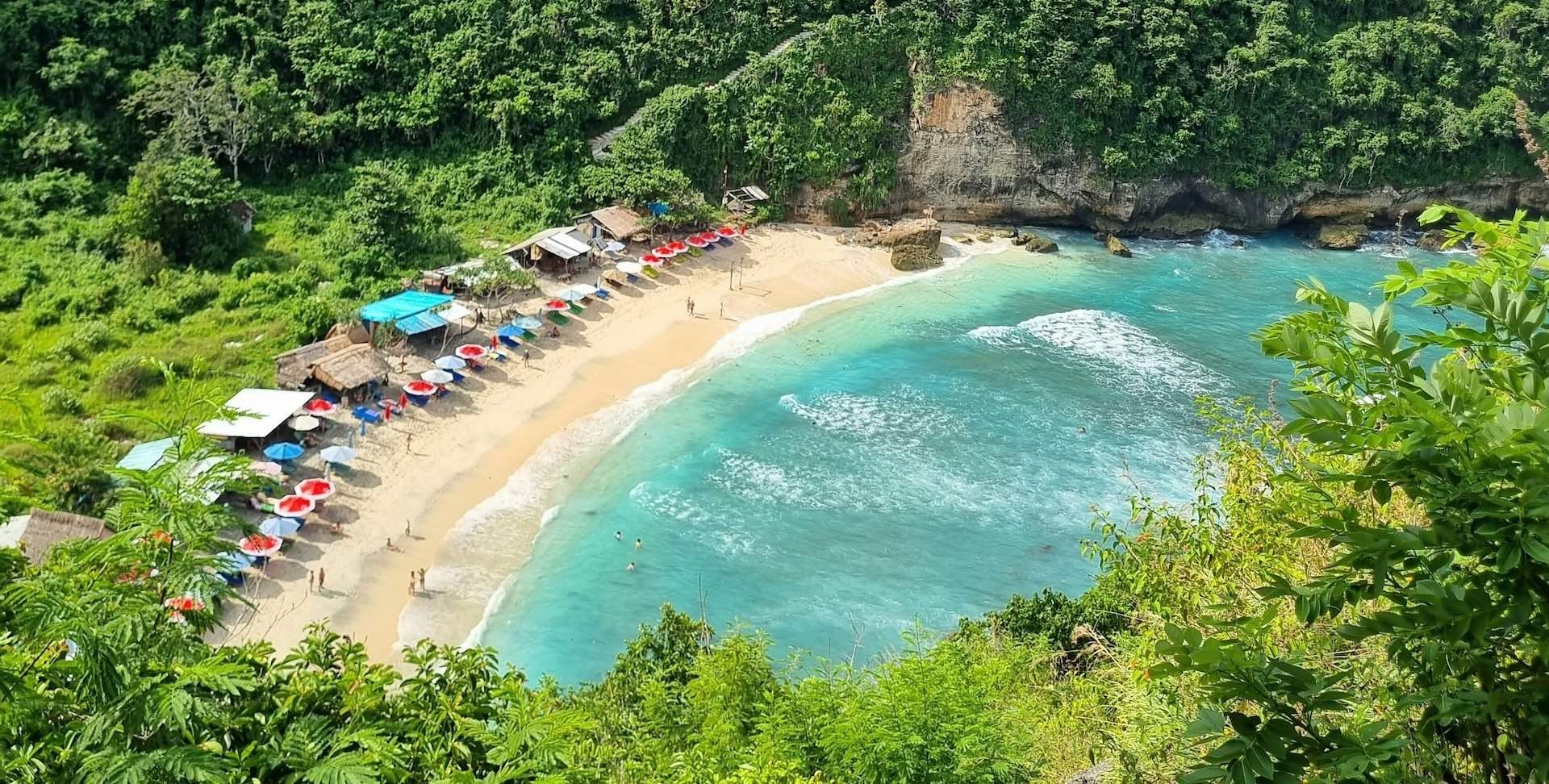 A beautiful white sand beach with turquoise water, seen from the top of a cliff.